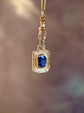 Gold pendant with a blue gemstone on a blurred background