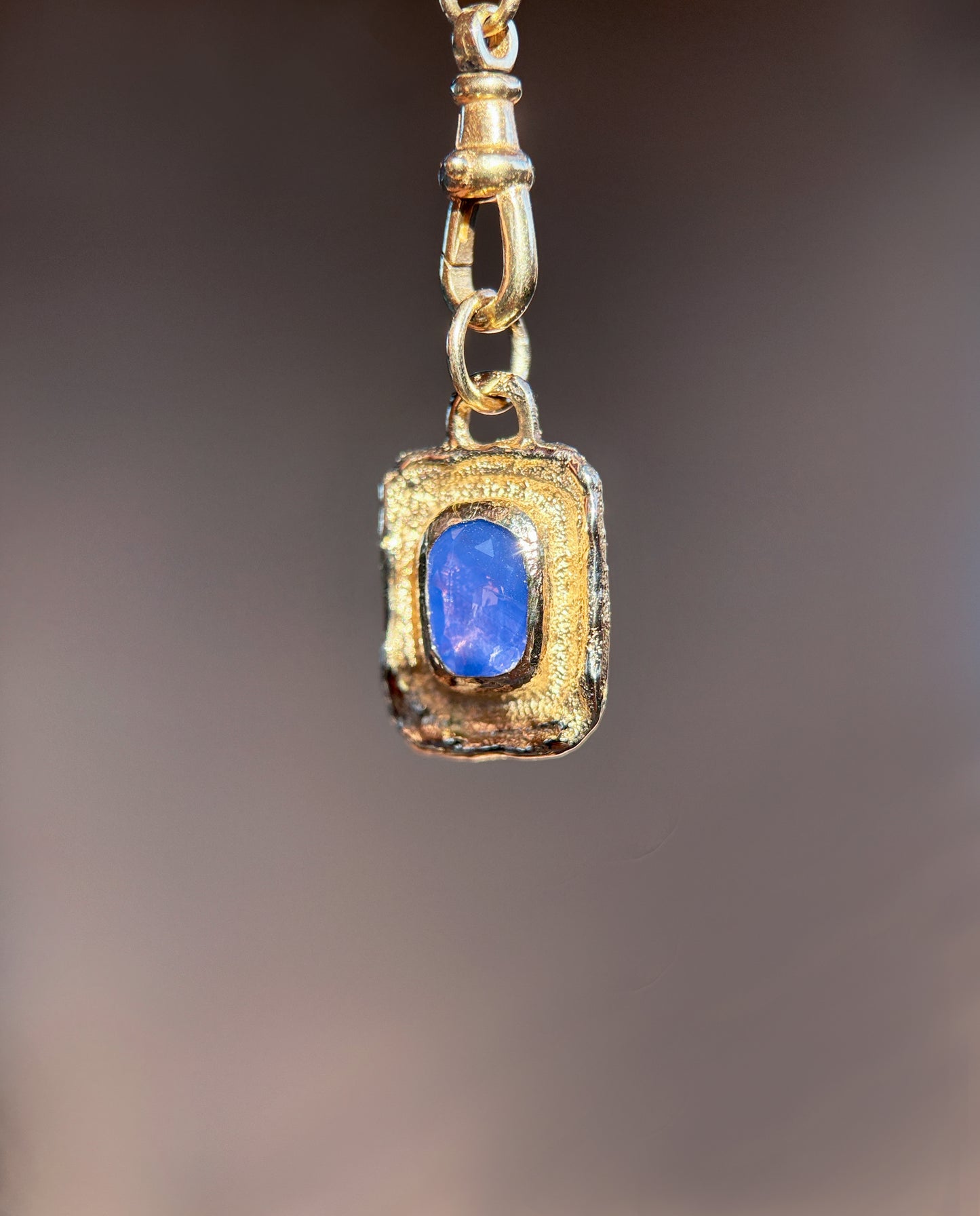 Gold pendant with a blue gemstone on a blurred background