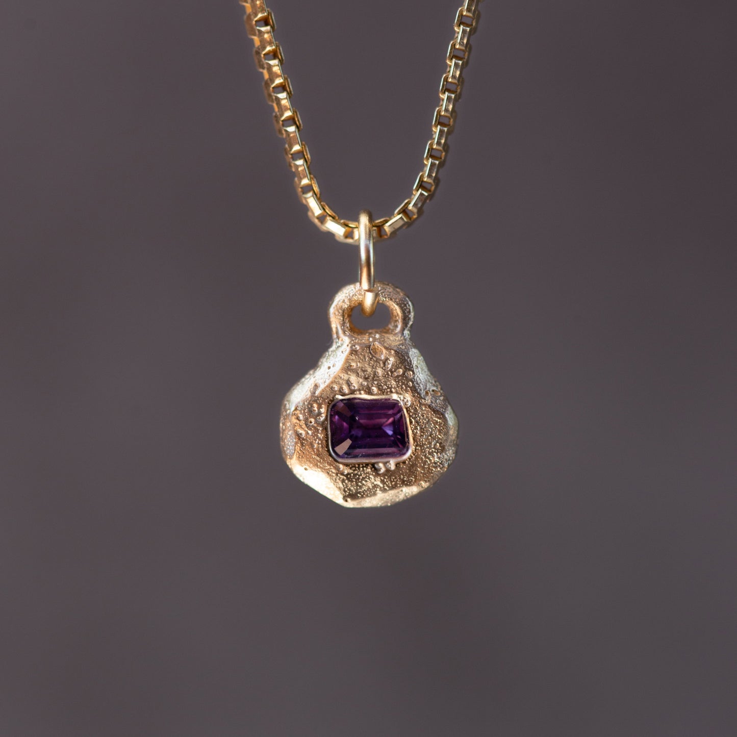 Gold necklace with a pendant featuring a purple gemstone on a dark background