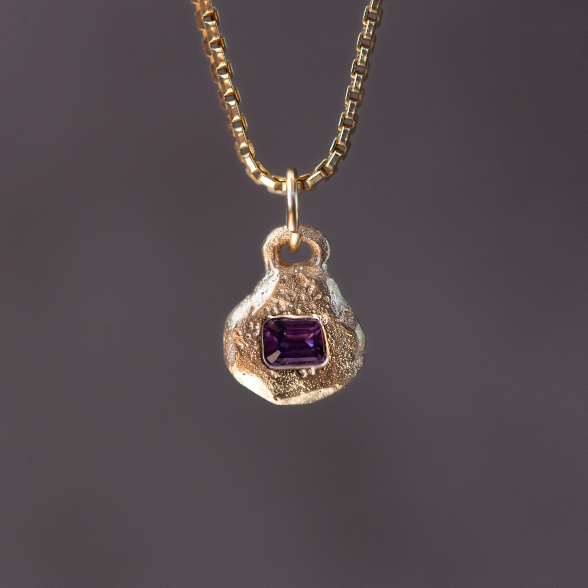 Gold necklace with a pendant featuring a purple gemstone on a dark background