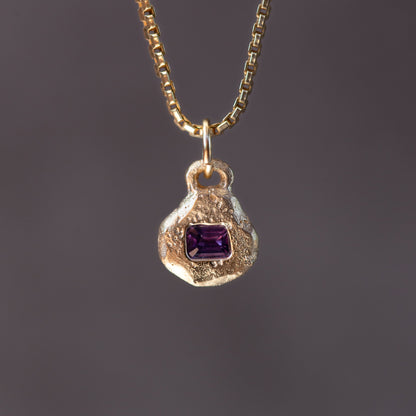 Gold necklace with a pendant featuring a purple gemstone on a dark background