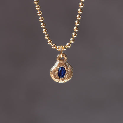 Gold necklace with a blue gemstone pendant on a dark gray background