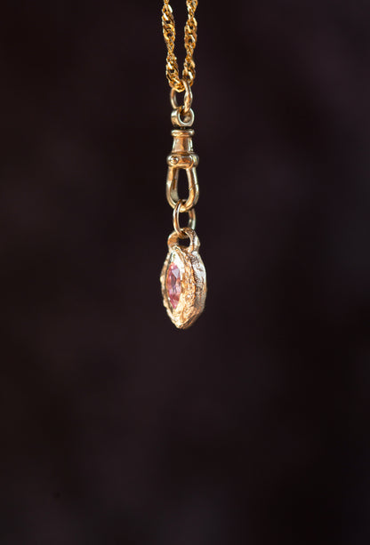 Gold necklace with a pink gemstone pendant on a dark background