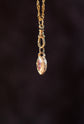 Gold necklace with a pink gemstone pendant on a dark background