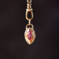 Gold pendant with a red gemstone on a dark background