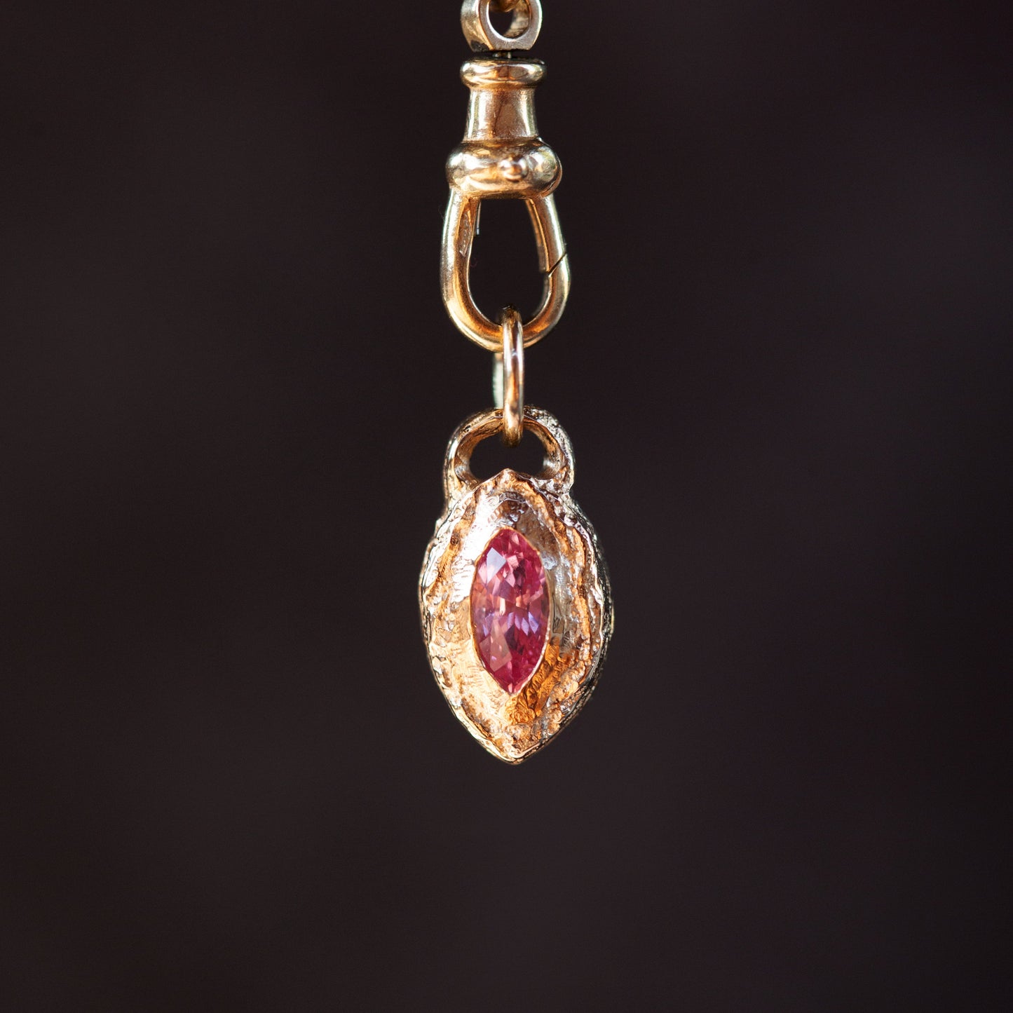 Gold pendant with a red gemstone on a dark background