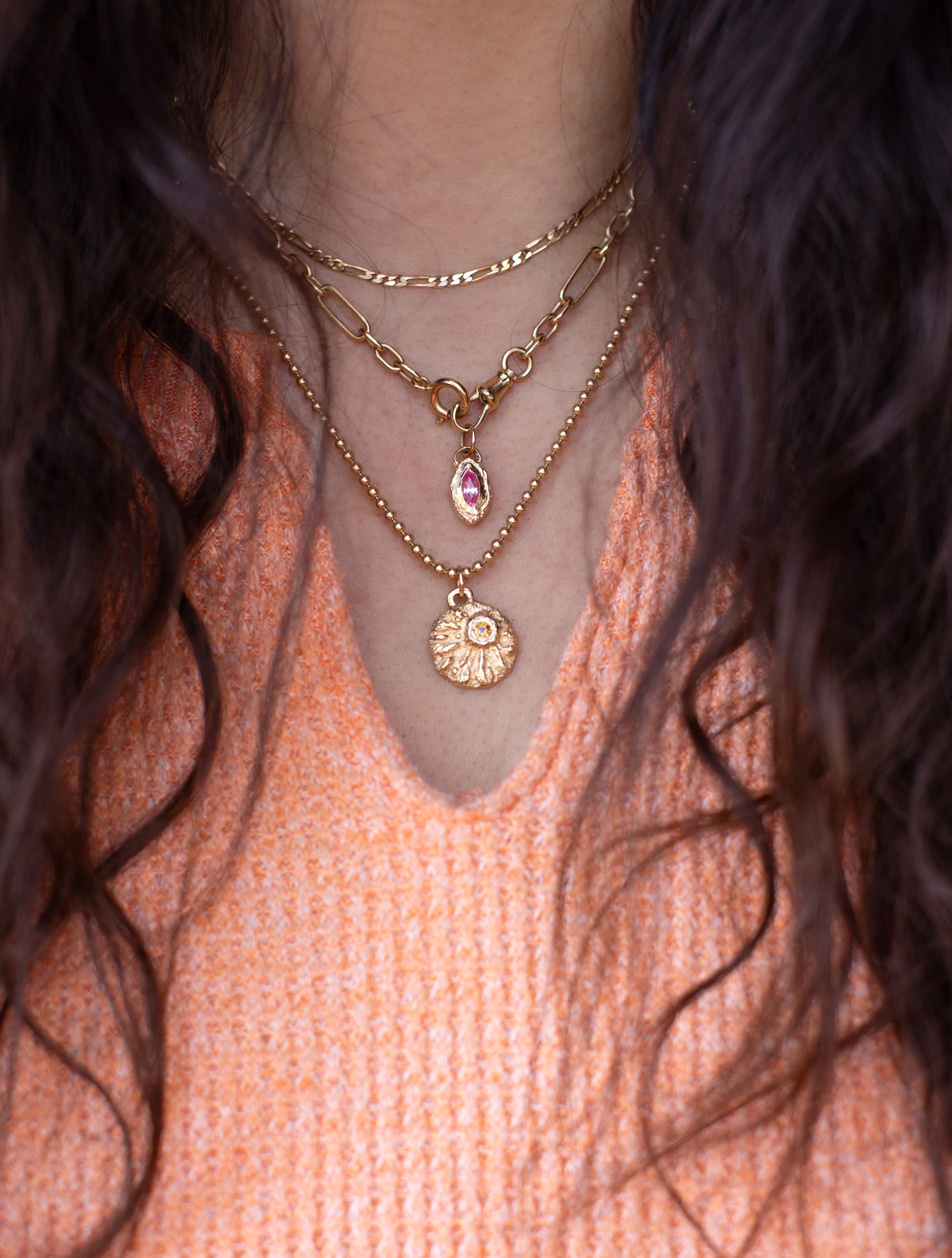 Close-up of a person wearing gold necklaces with a pink top and dark hair.