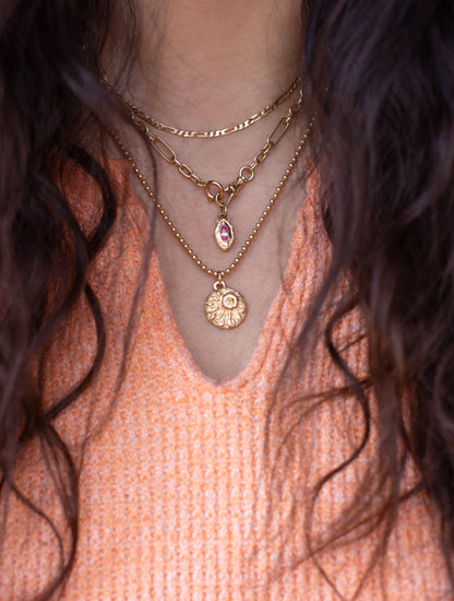 Close-up of a person wearing gold necklaces with a pink top and dark hair.
