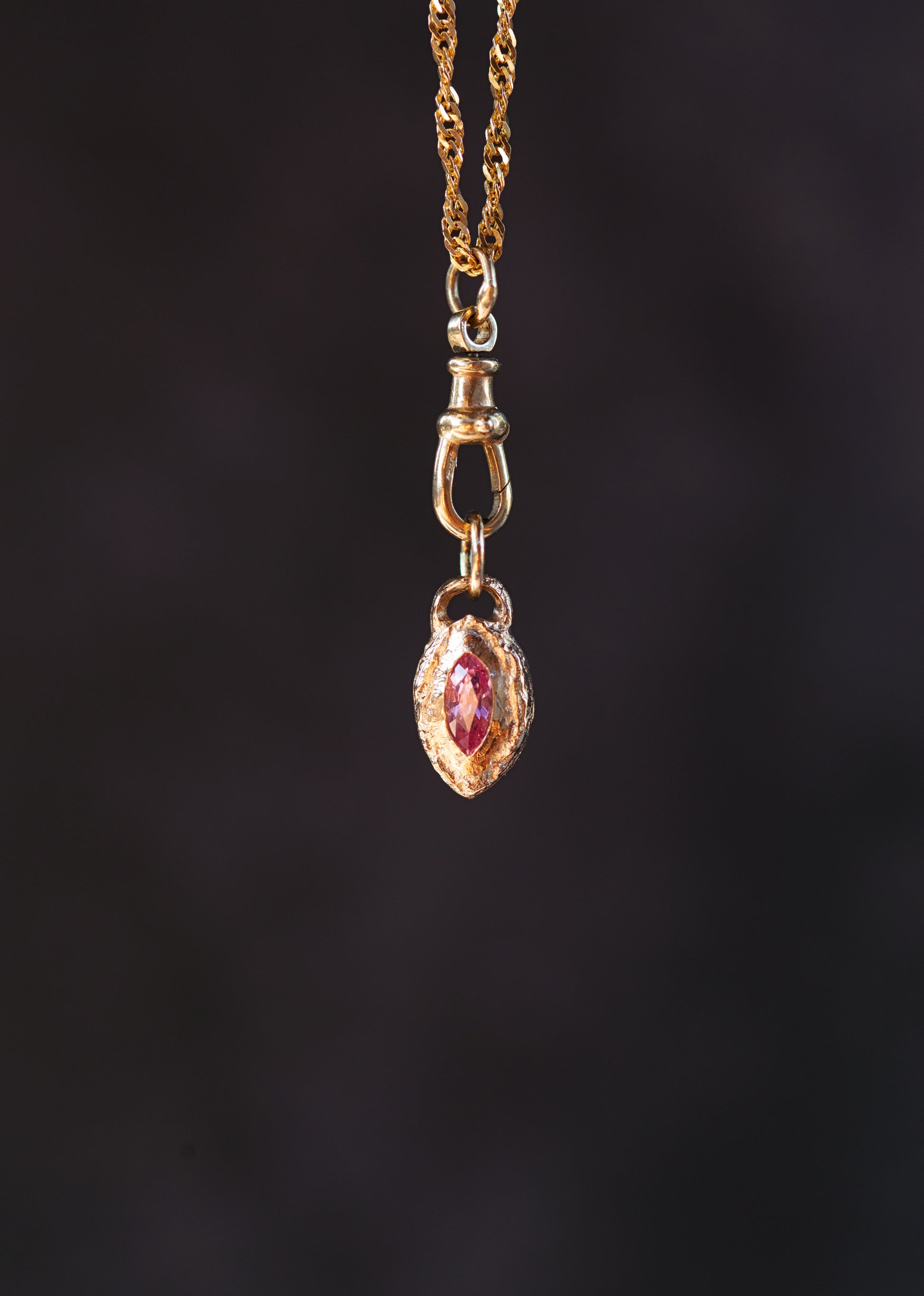 Gold necklace with a pendant featuring a red gemstone on a dark background