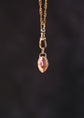 Gold necklace with a pendant featuring a red gemstone on a dark background