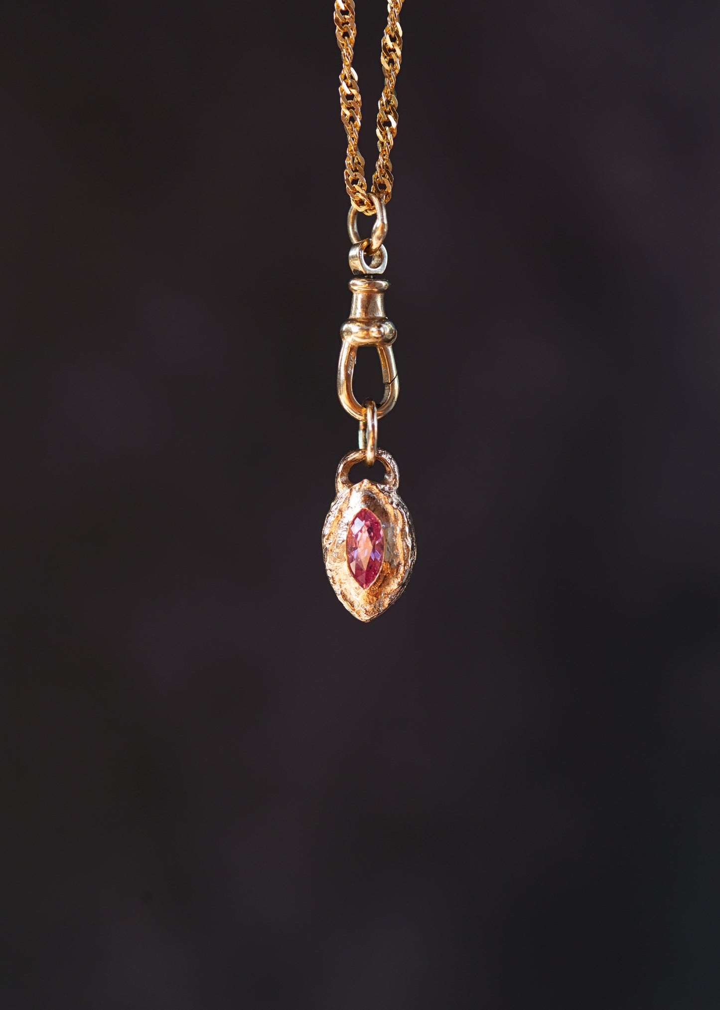 Gold necklace with a pendant featuring a red gemstone on a dark background