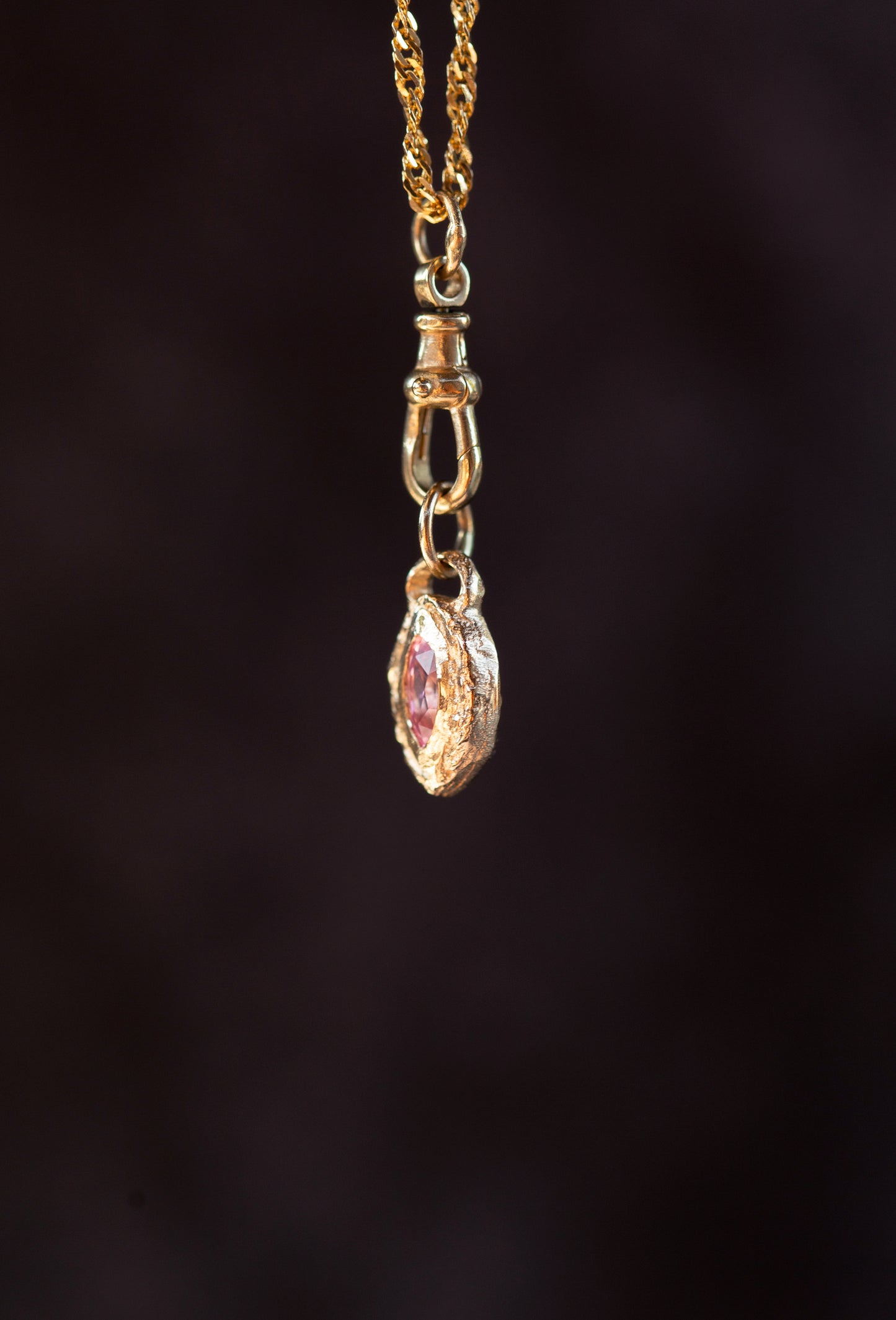 Gold necklace with a pink gemstone pendant on a dark background