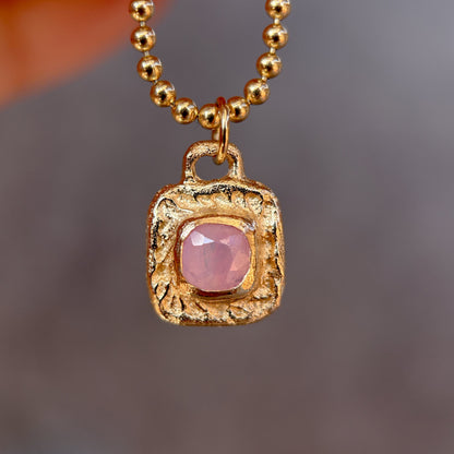 Gold necklace with a pink gemstone pendant against a blurred background