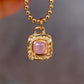 Gold necklace with a pink gemstone pendant against a blurred background
