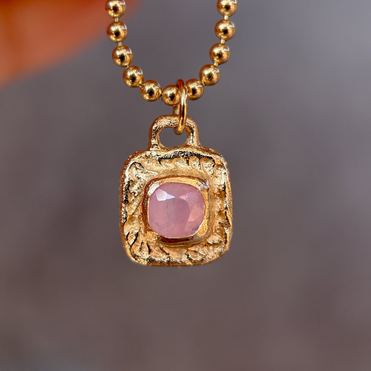 Gold necklace with a pink gemstone pendant against a blurred background