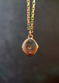 Gold necklace with a textured pendant on a dark background