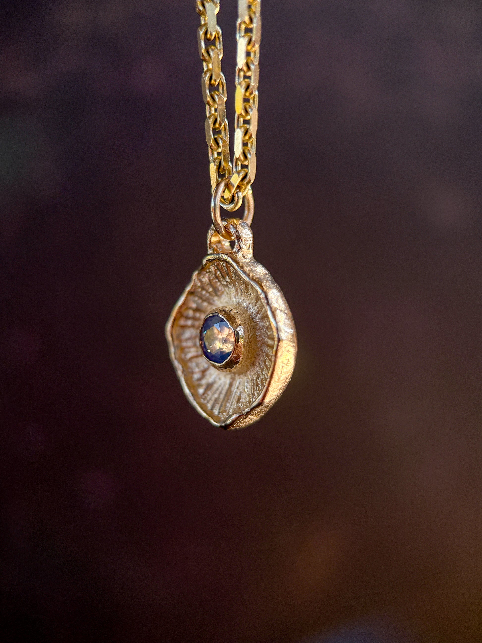 Gold necklace with a pendant featuring a blue gemstone on a dark background