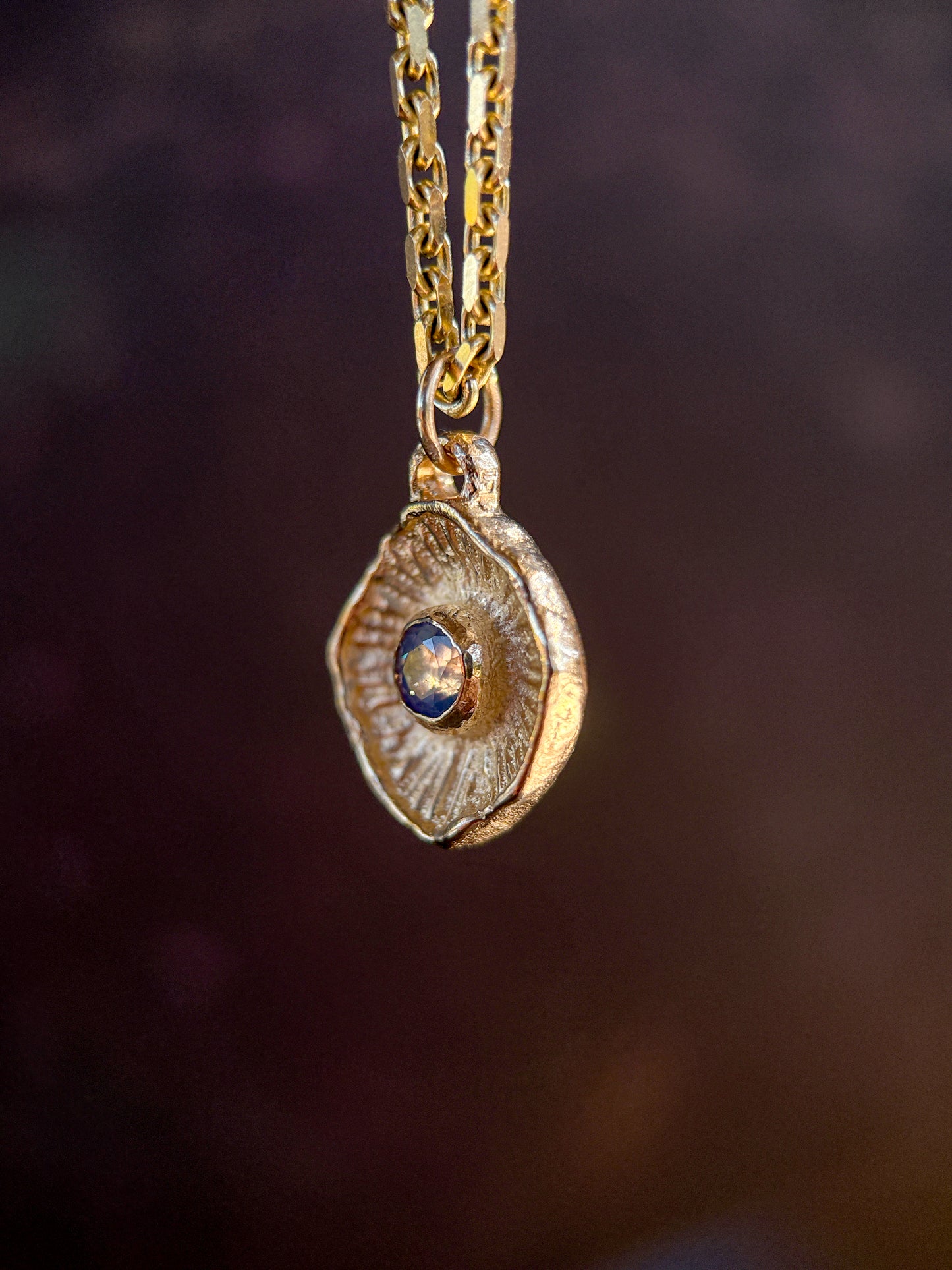 Gold necklace with a pendant featuring a blue gemstone on a dark background