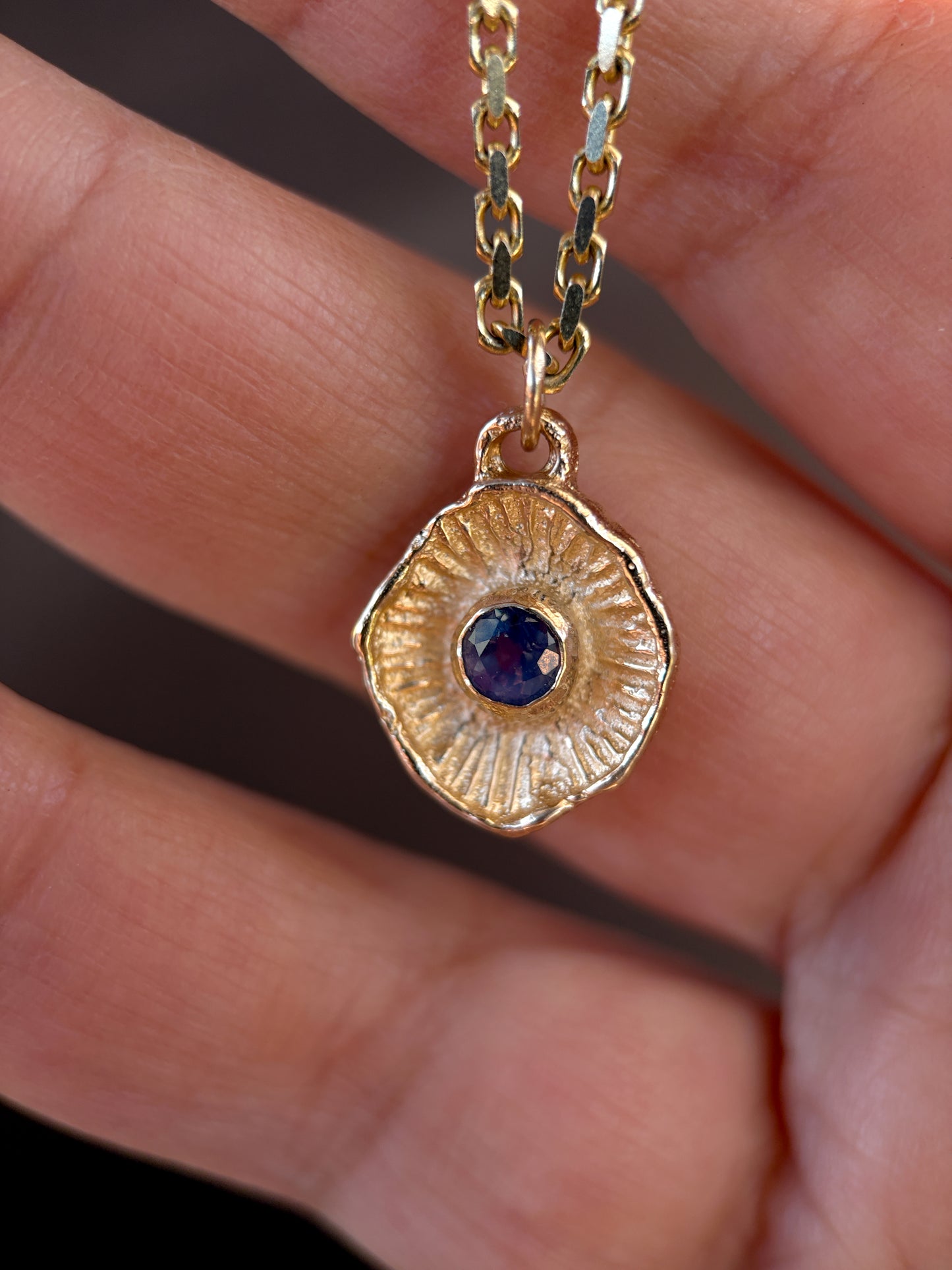 Gold necklace with a pendant featuring a blue gemstone held between fingers.