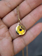 A gold-toned necklace with a circular pendant featuring a central black dot, held in a person's hand.