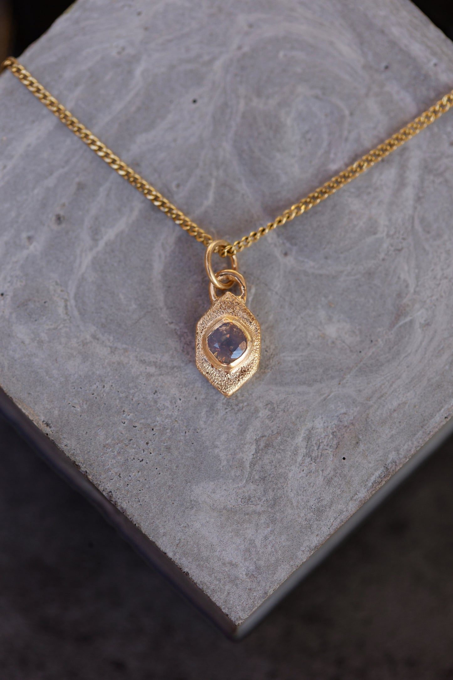 Gold necklace with a pendant on a gray stone surface