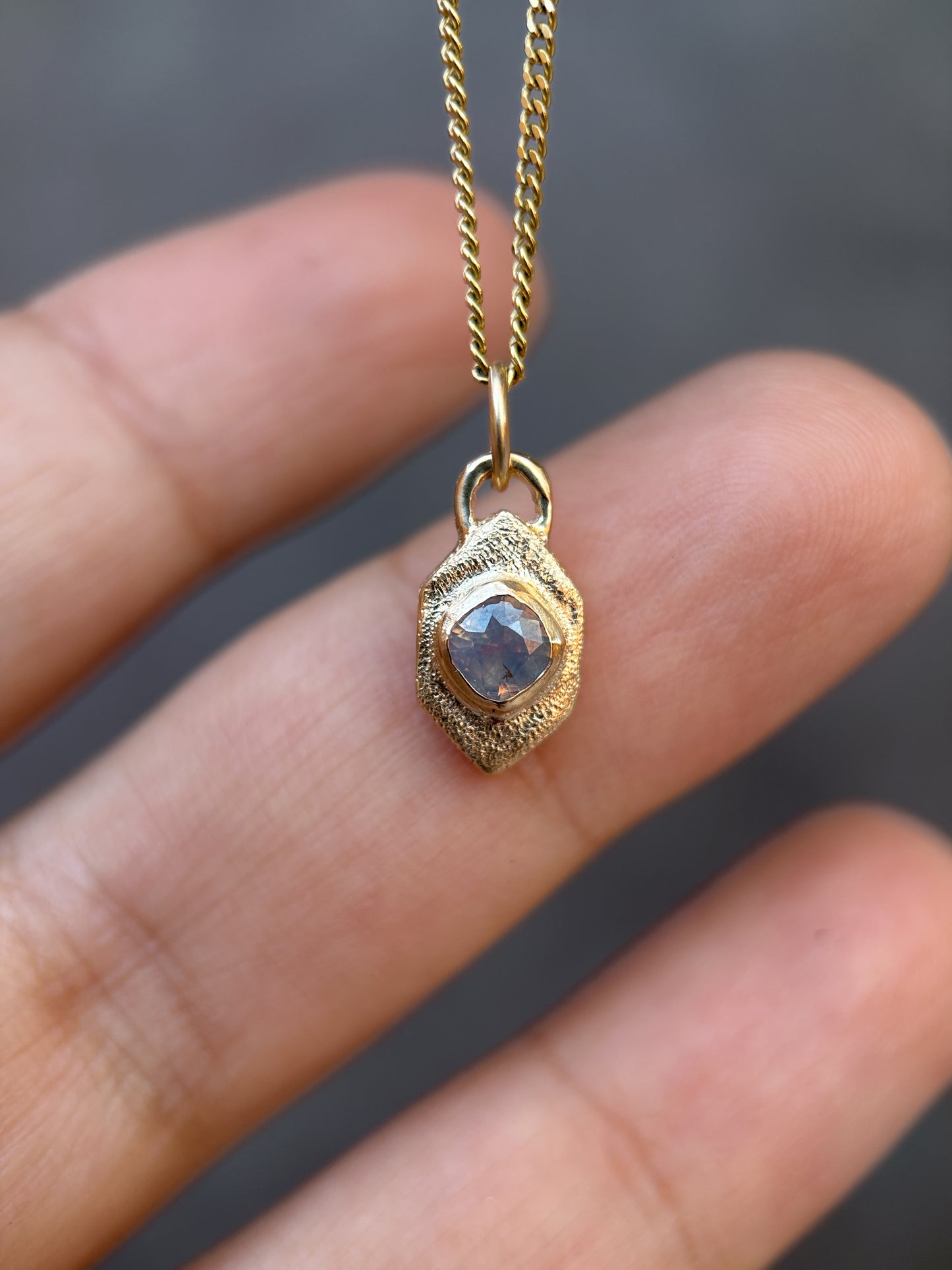 Gold pendant with a blue stone held between fingers against a blurred background