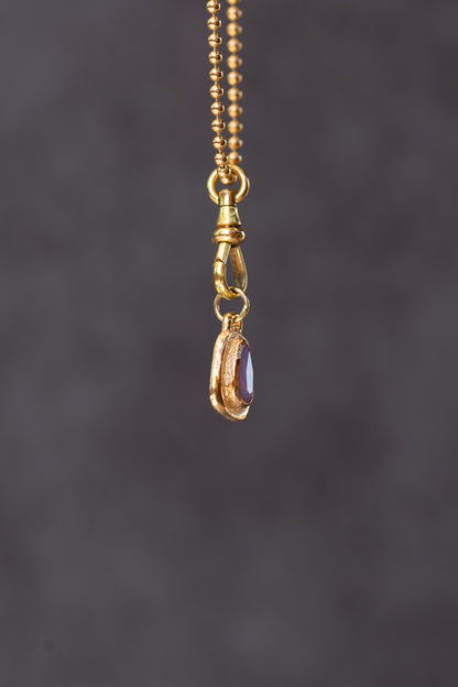 Gold necklace with a pendant featuring a purple gemstone on a dark gray background