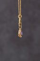 Gold necklace with a pendant featuring a purple gemstone on a dark gray background