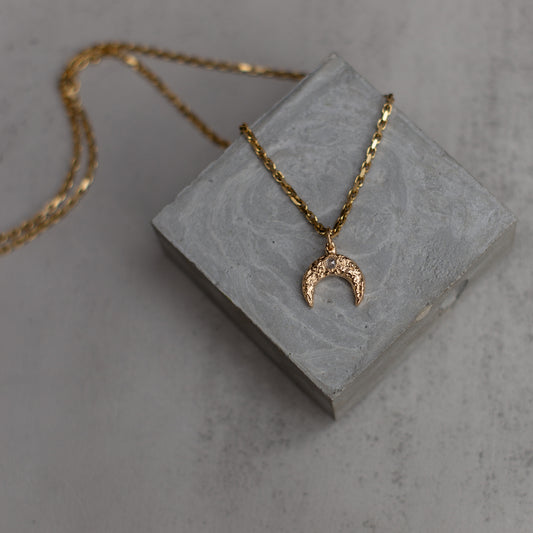 Gold necklace with a crescent moon pendant on a gray stone surface