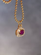 Gold necklace with a pendant featuring a red gemstone on a blurred background