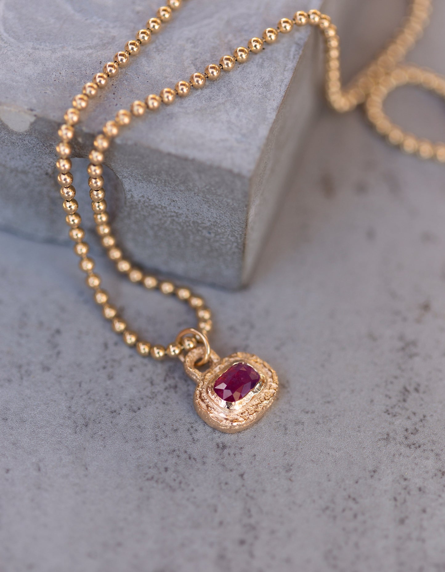 Gold necklace with a red gemstone pendant on a gray surface