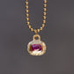 Gold necklace with a pendant featuring a red gemstone on a dark background