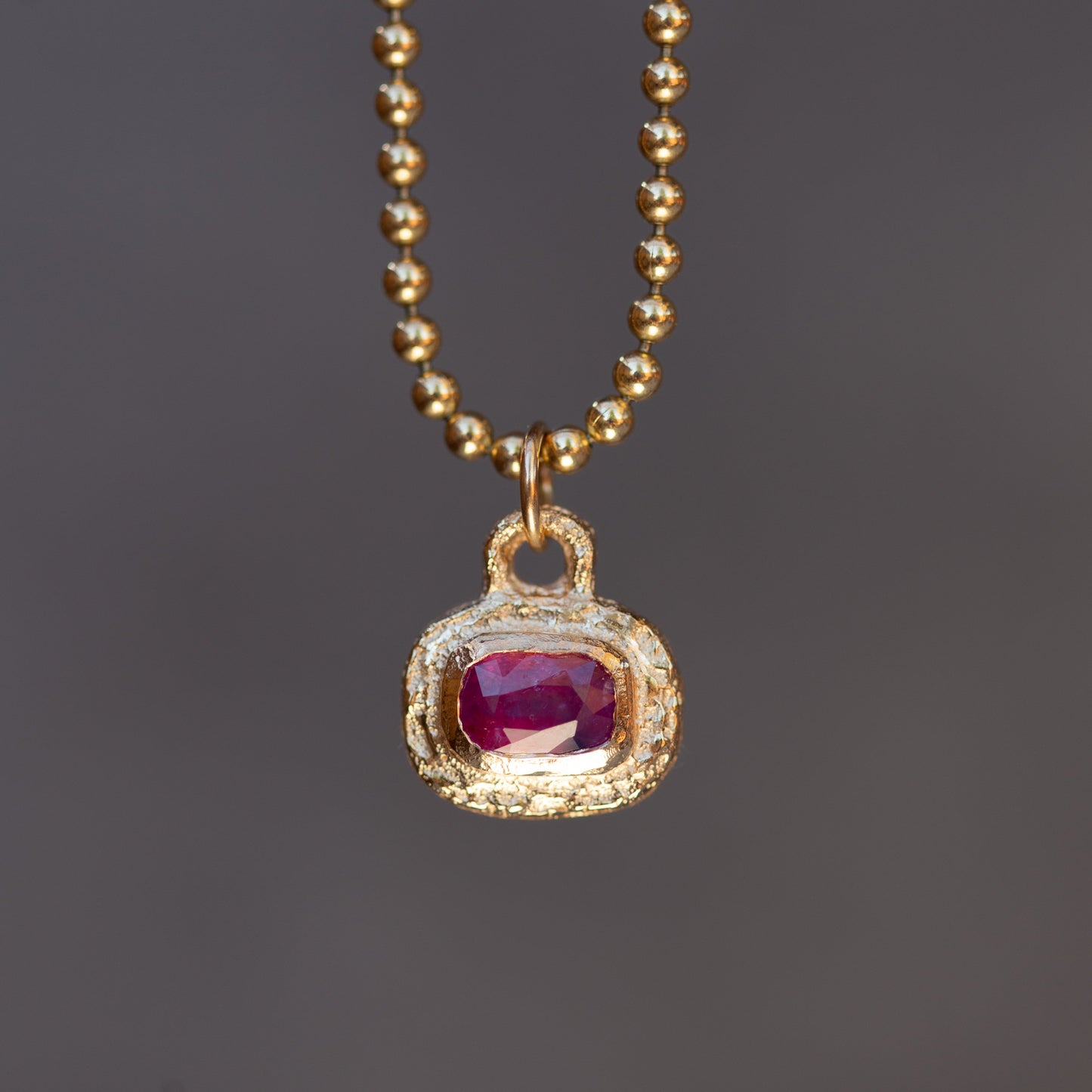Gold necklace with a pendant featuring a red gemstone on a dark background