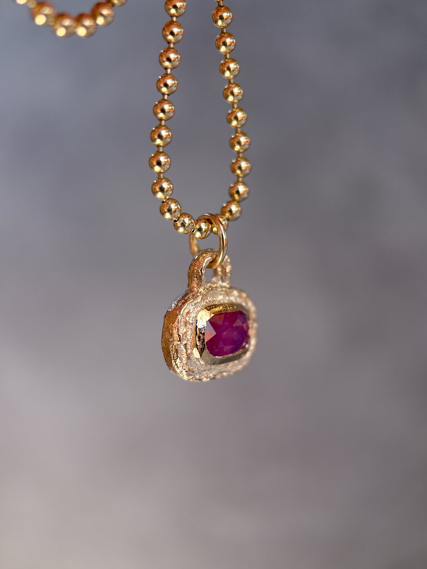 Gold necklace with a pendant featuring a red gemstone on a blurred background
