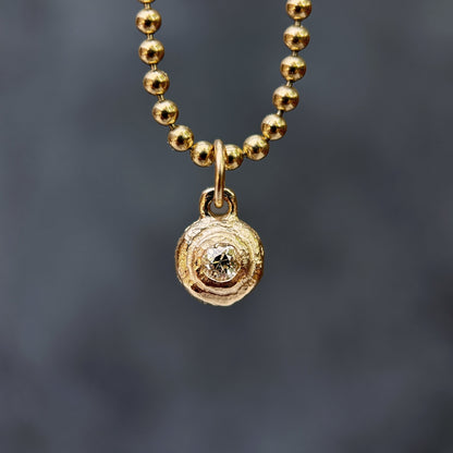 Gold beaded necklace with a circular pendant on a dark gray background