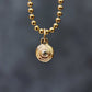 Gold beaded necklace with a circular pendant on a dark gray background