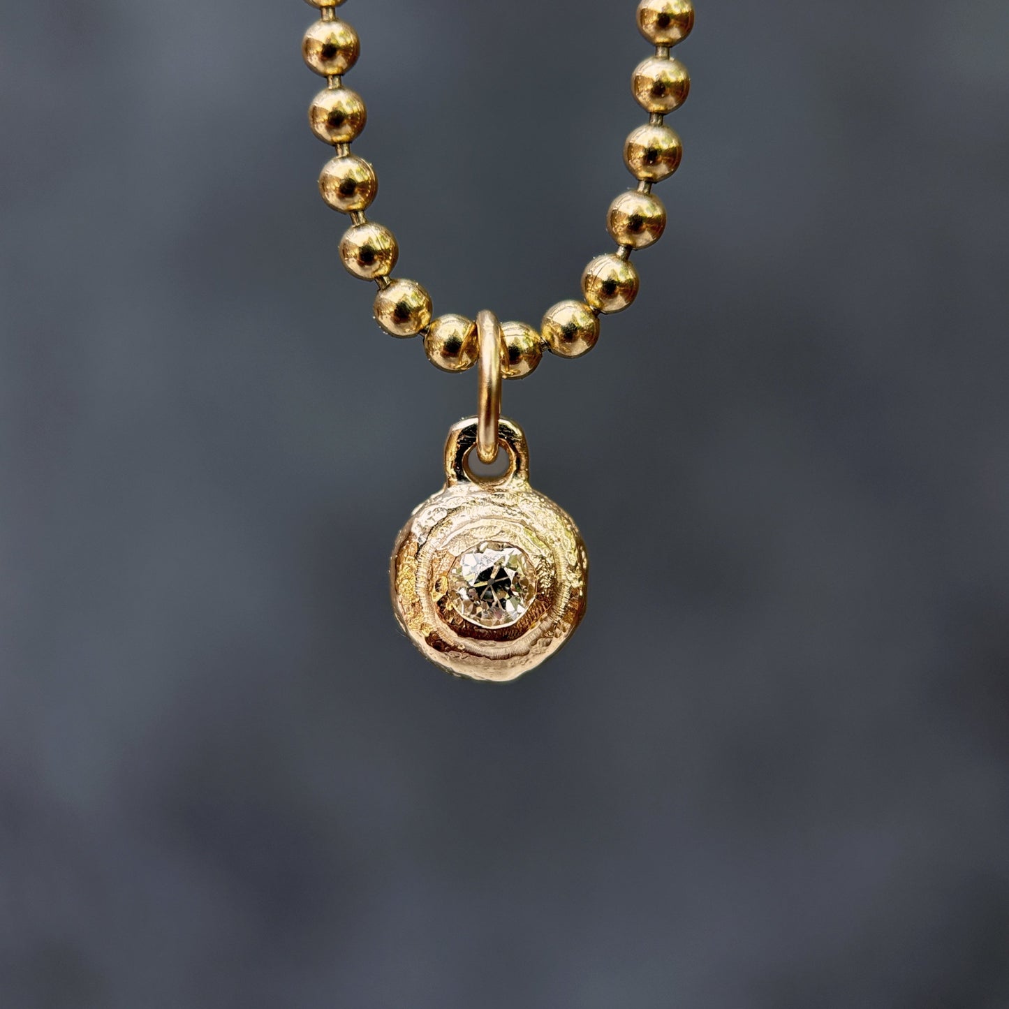 Gold beaded necklace with a circular pendant on a dark gray background
