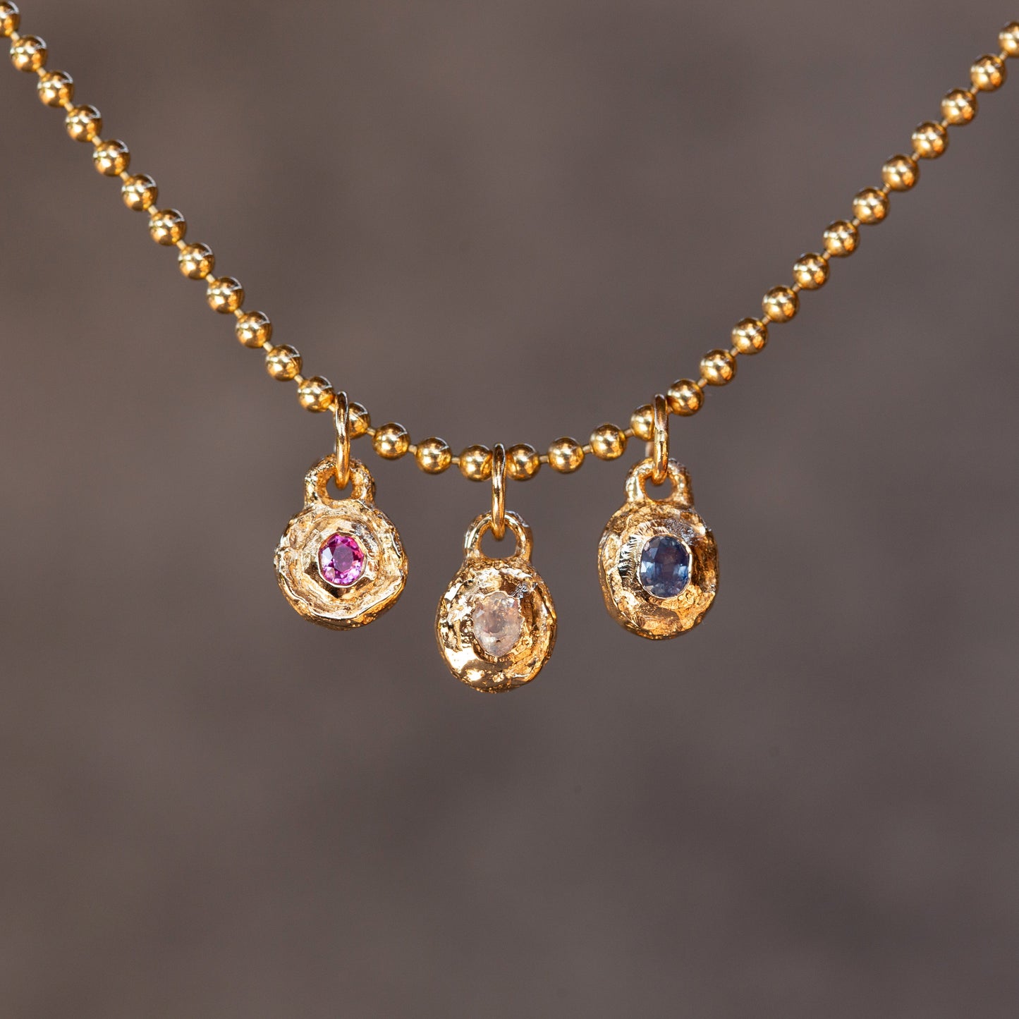 Gold necklace with three pendant charms on a dark background
