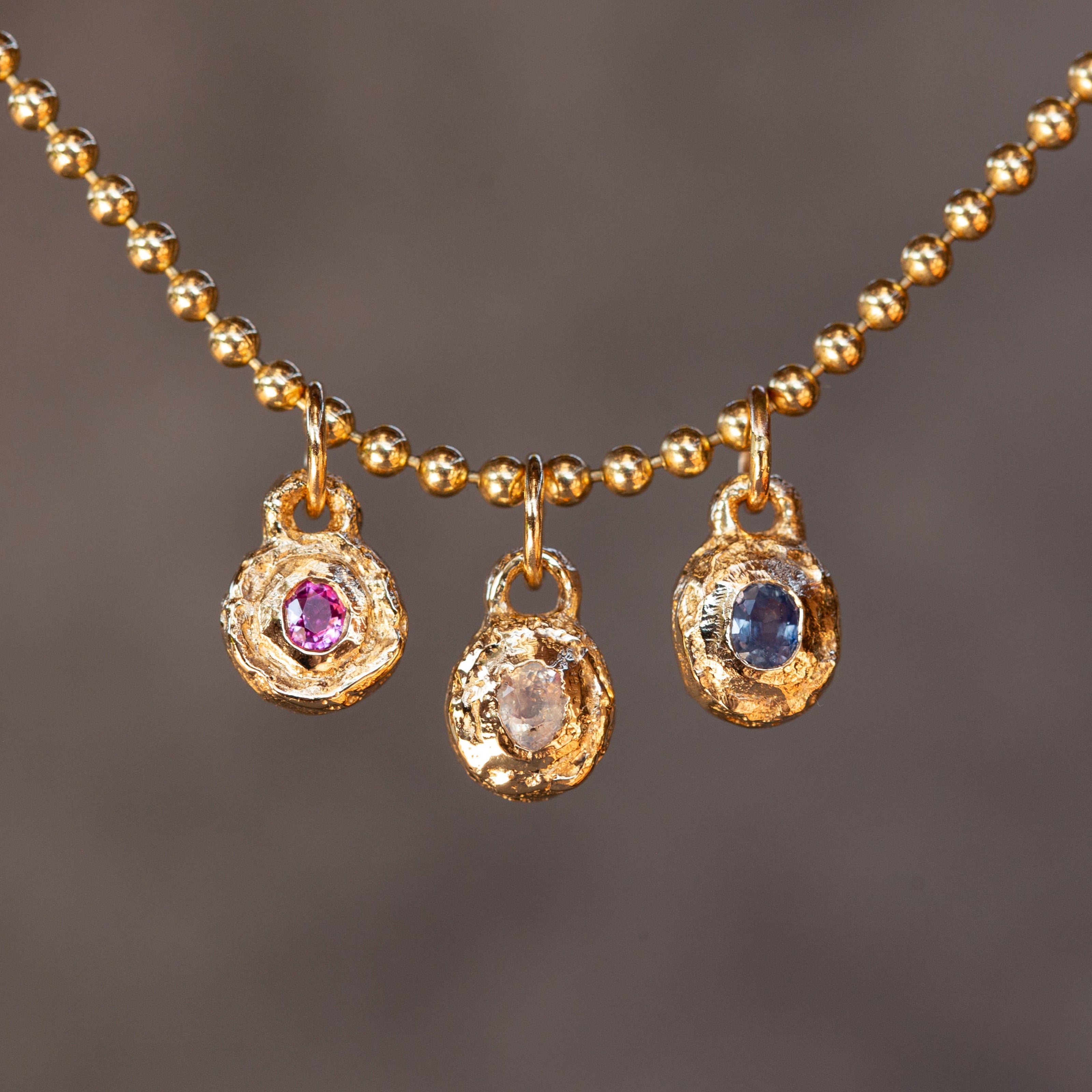 Gold necklace with three pendant charms on a dark background