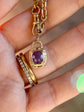 Gold necklace with a purple gemstone pendant held by a hand.