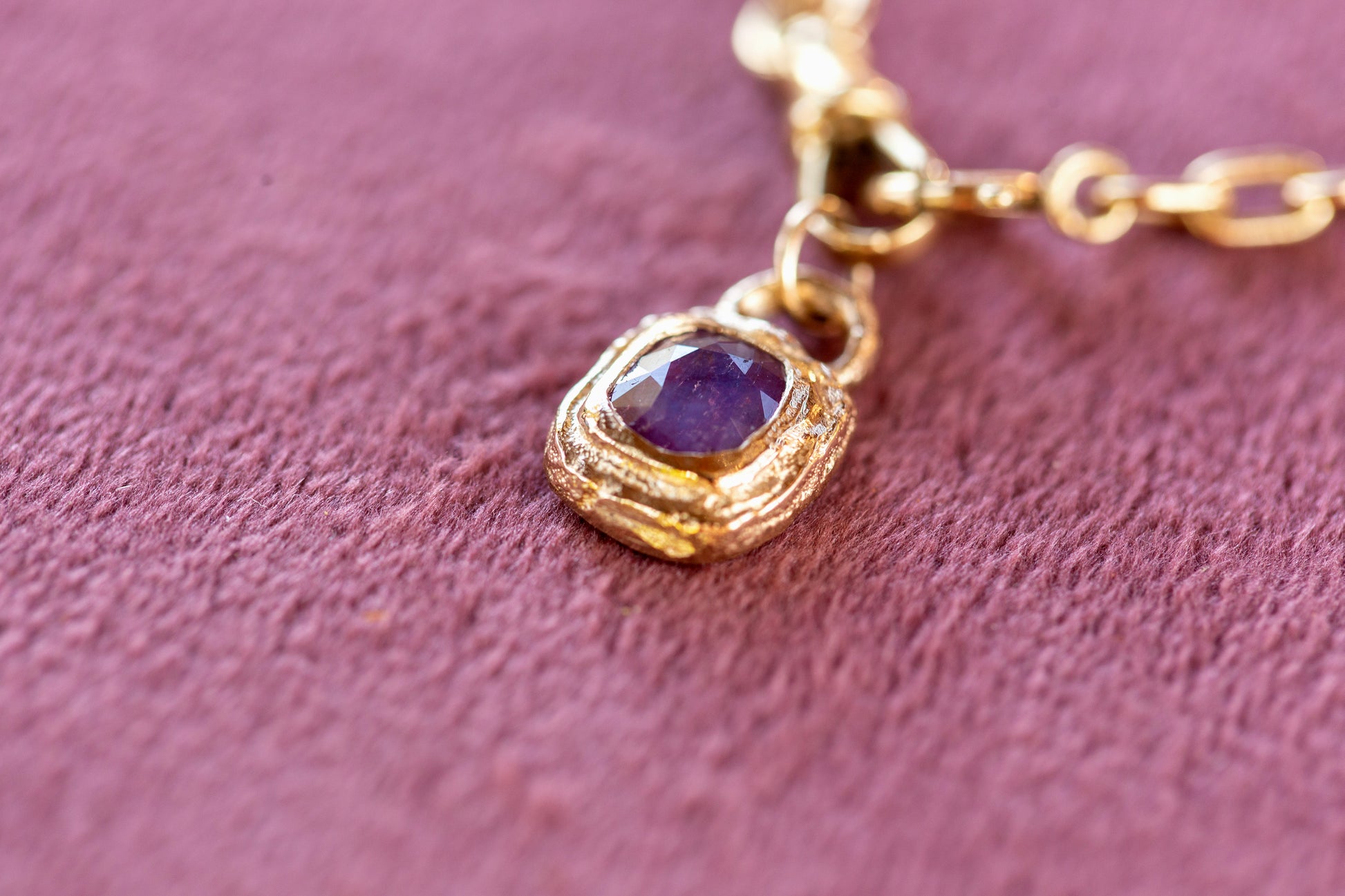 Gold necklace with a purple gemstone pendant on a pink textured background