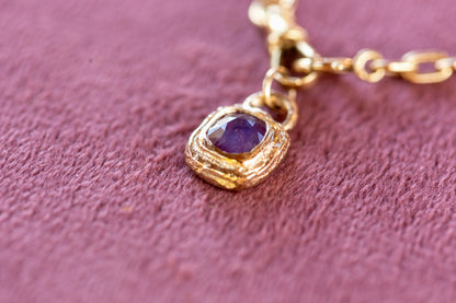 Gold necklace with a purple gemstone pendant on a pink textured background