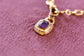 Gold necklace with a purple gemstone pendant on a pink textured background