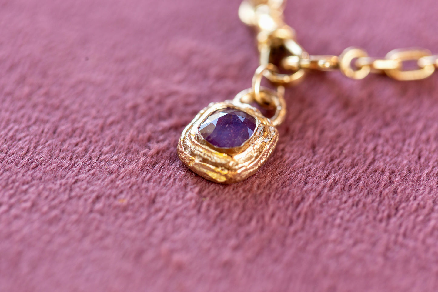 Gold necklace with a purple gemstone pendant on a pink textured background