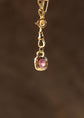 Gold pendant with a pink gemstone on a dark brown background