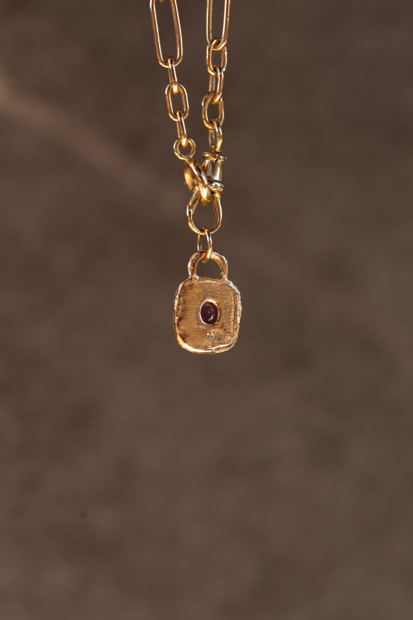 Gold necklace with a square pendant on a brown background