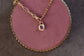 Gold necklace with a purple gemstone pendant on a pink textured surface