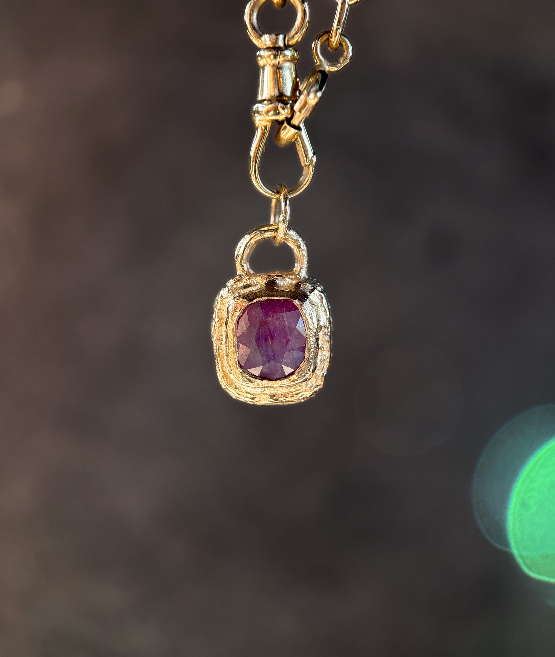 Gold pendant with a red gemstone on a dark background