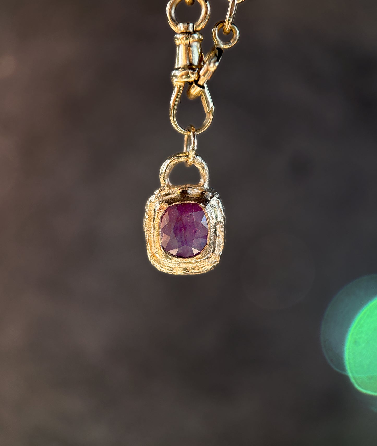 Gold pendant with a red gemstone on a dark background