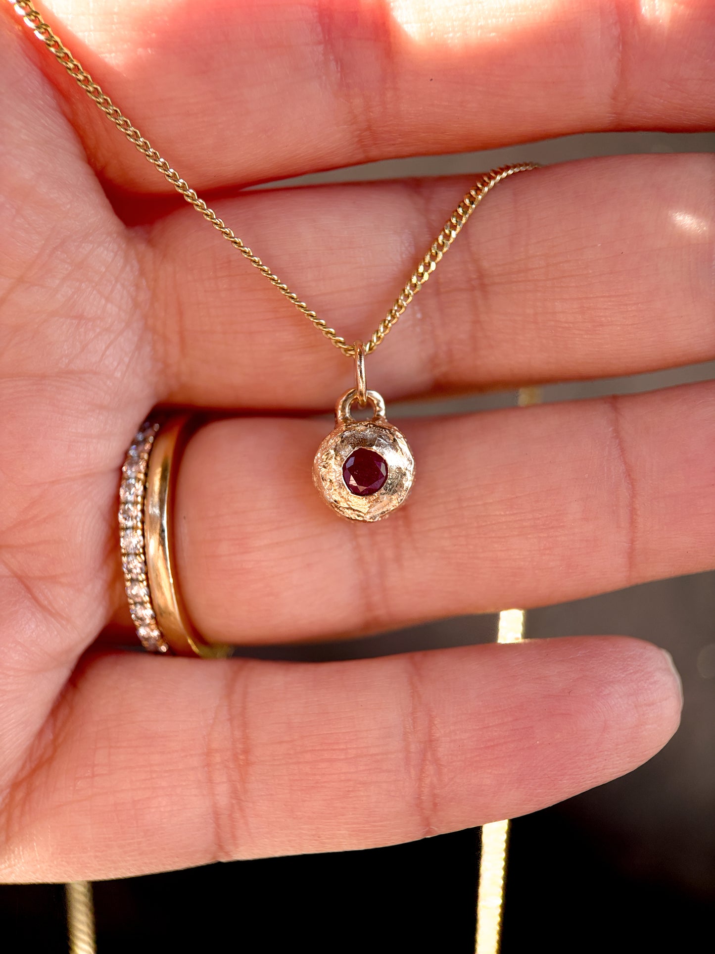Gold necklace with a red gemstone pendant held by a hand.